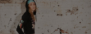 Woman in a floral cropped zip hoodie and headband posing against a rustic wall for an urban street look.