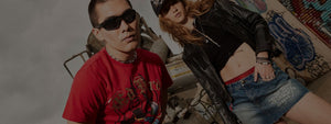 Man in graphic tee and woman in denim skirt and leather jacket showcasing bold 2000s street style.
